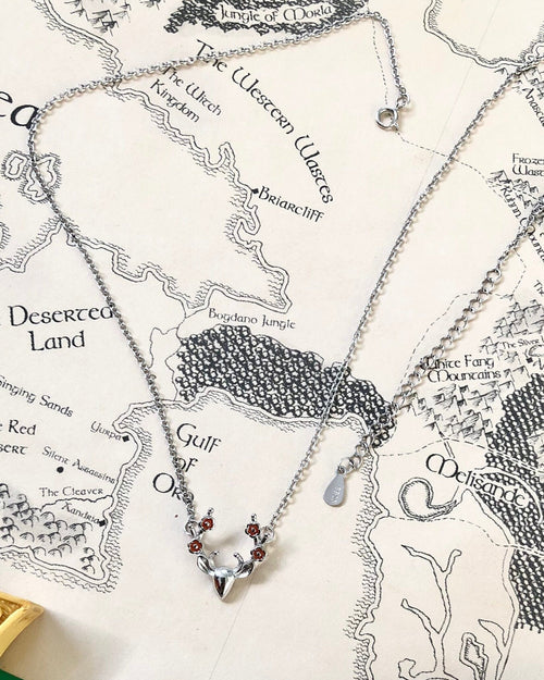 A sterling silver necklace with a pendant featuring antlers and four blossoms, displayed on a fantasy map 