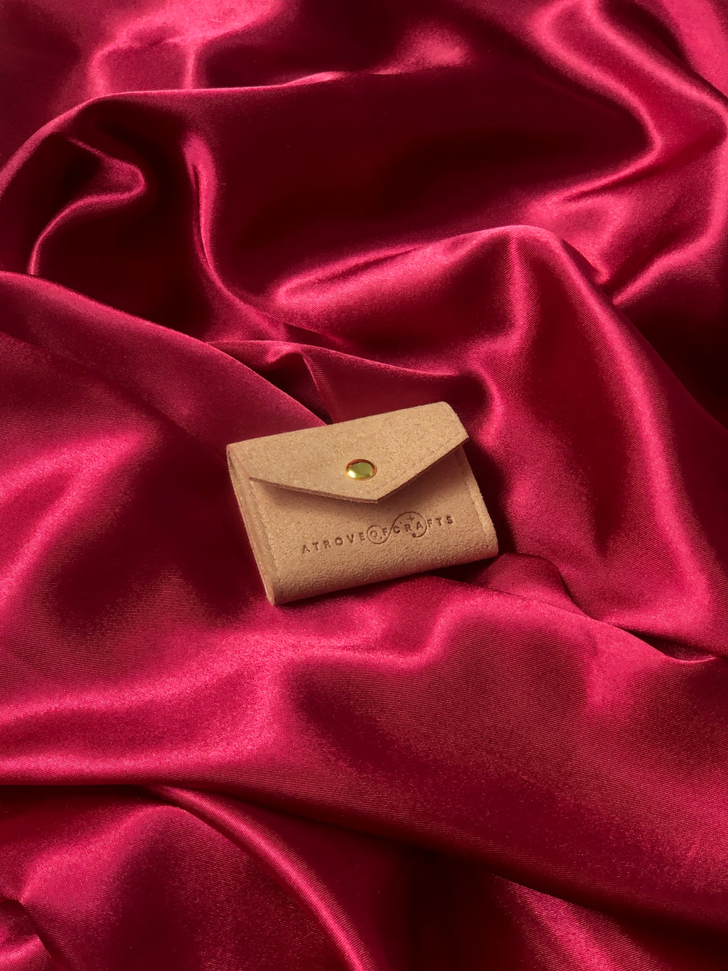 Travel sized light pink pouch with a brand logo on a red satin background
