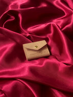 Travel sized light pink pouch with a brand logo on a red satin background