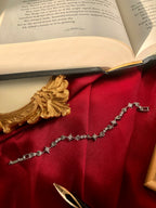 Silver tennis bracelet with star charms on a red fabric background next to an open book.