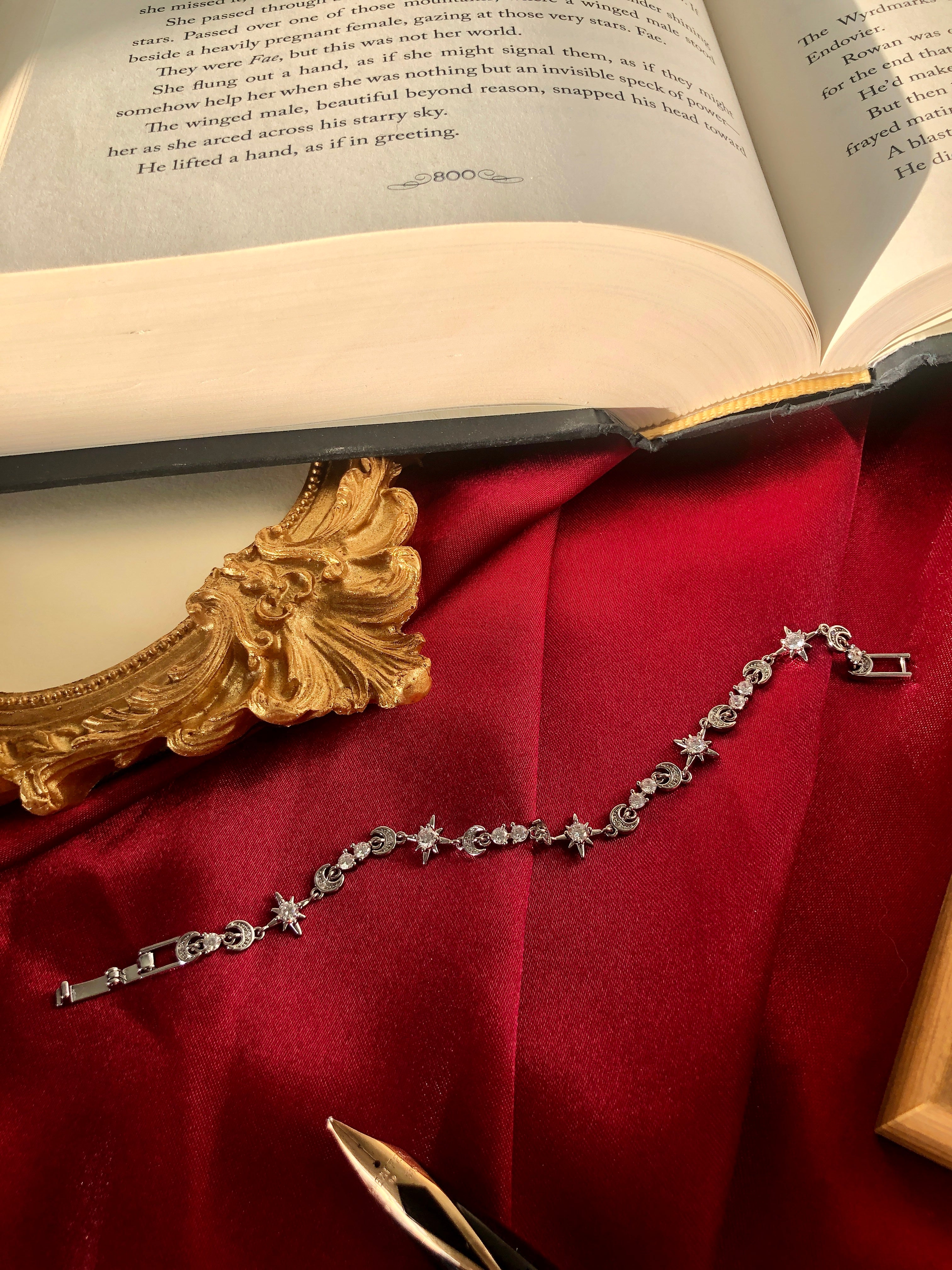 Silver tennis bracelet with star charms on a red fabric background next to an open book.