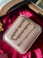 Gold adjustable charm bracelet with colorful beads in a jewelry box on a red fabric background