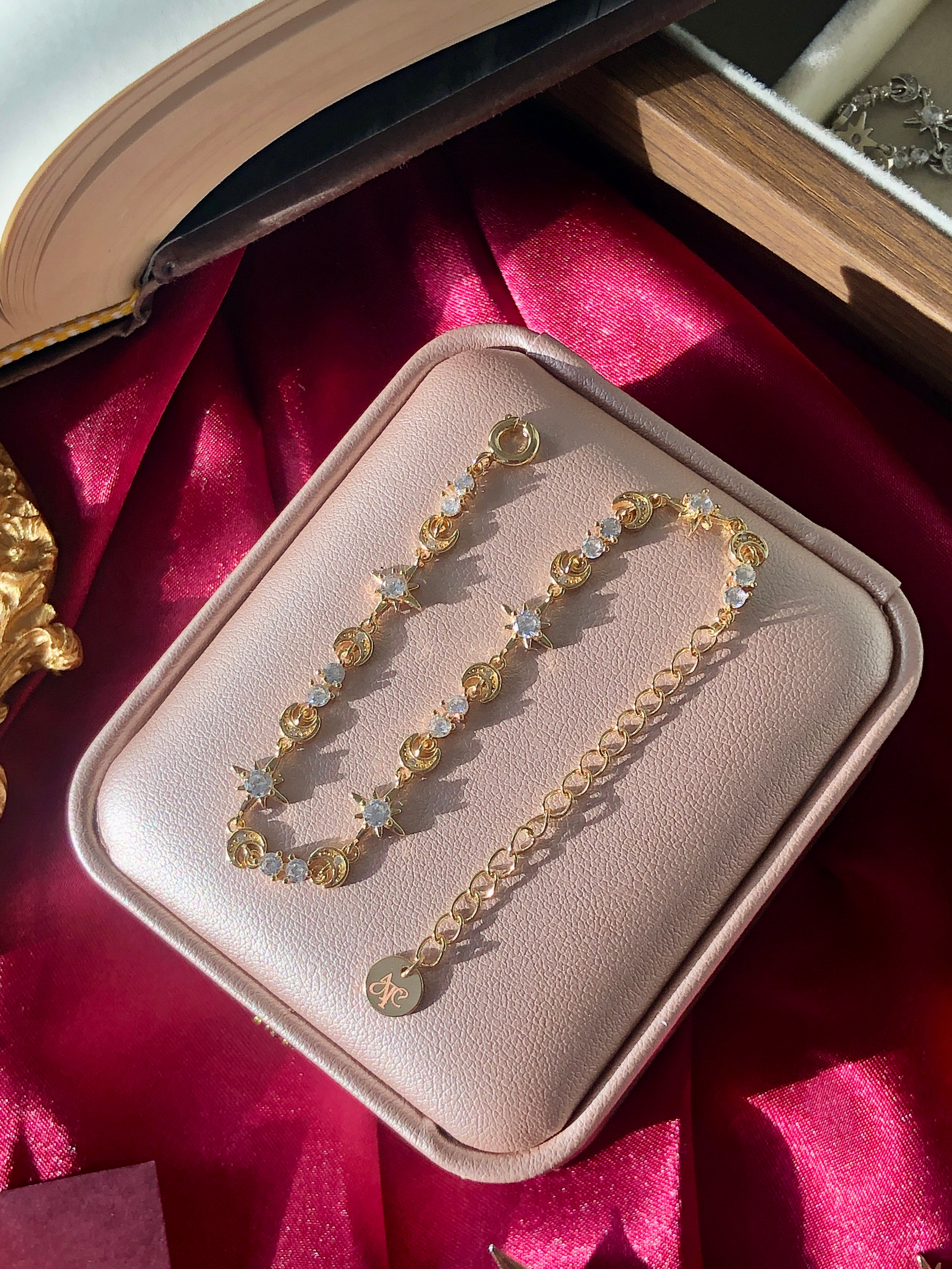 Gold adjustable charm bracelet with colorful beads in a jewelry box on a red fabric background