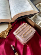 Pink jewelry box with gold bracelets on a red fabric background with an open book and fountain pen.
