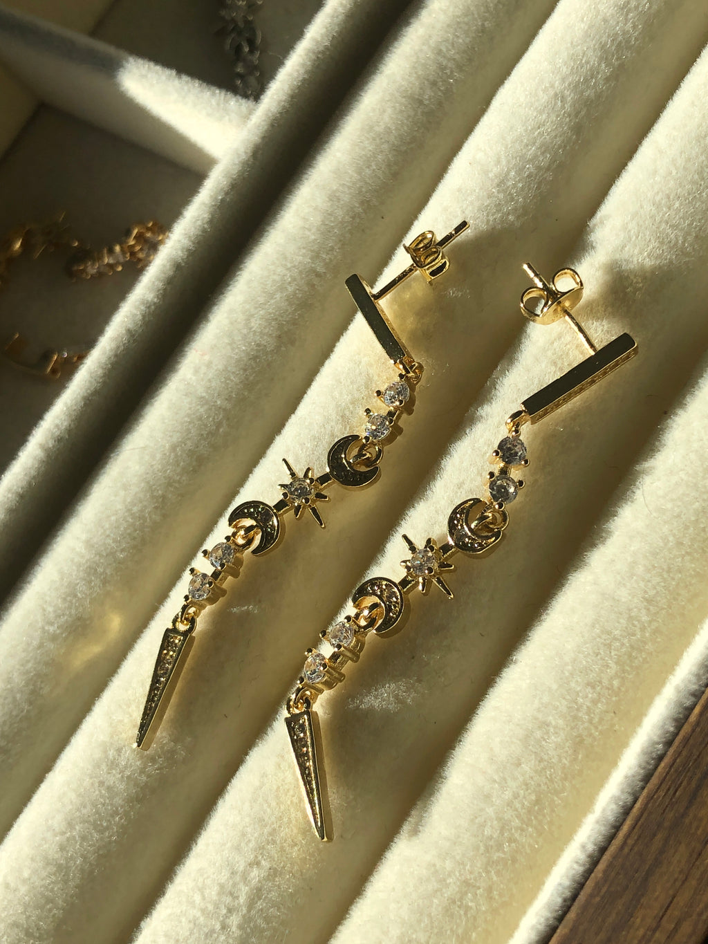 Gold earrings with star and moon designs on a beige surface