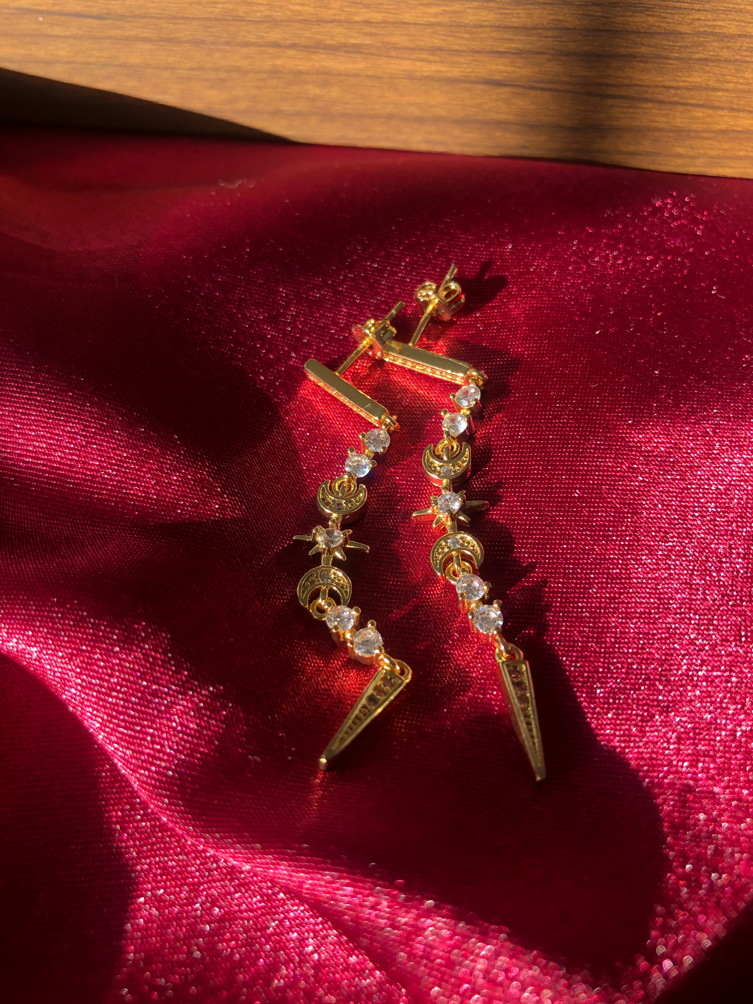 Gold star and moon earrings with gemstones on a red fabric background