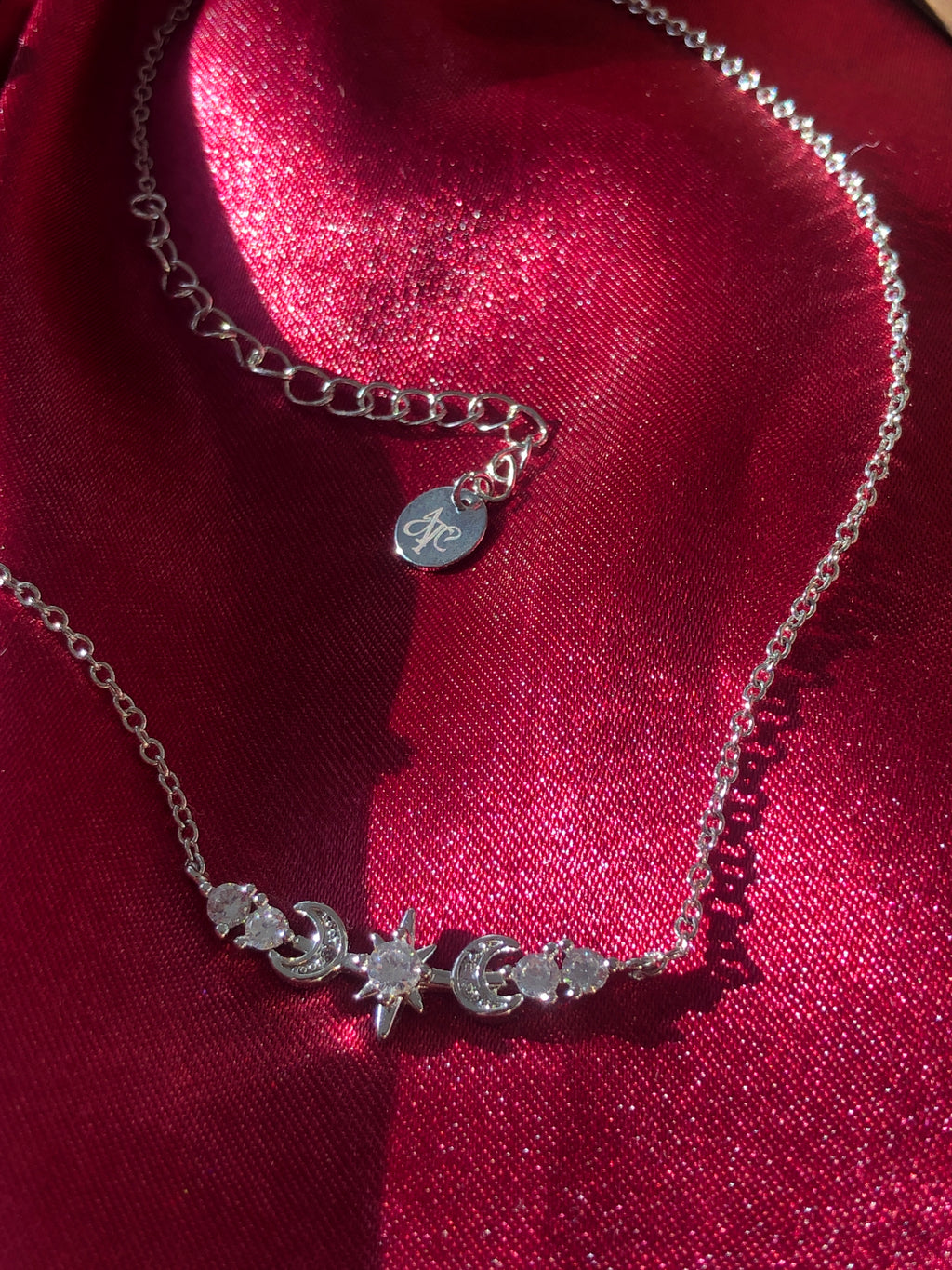 Silver necklace with star and moon charms on a red fabric background