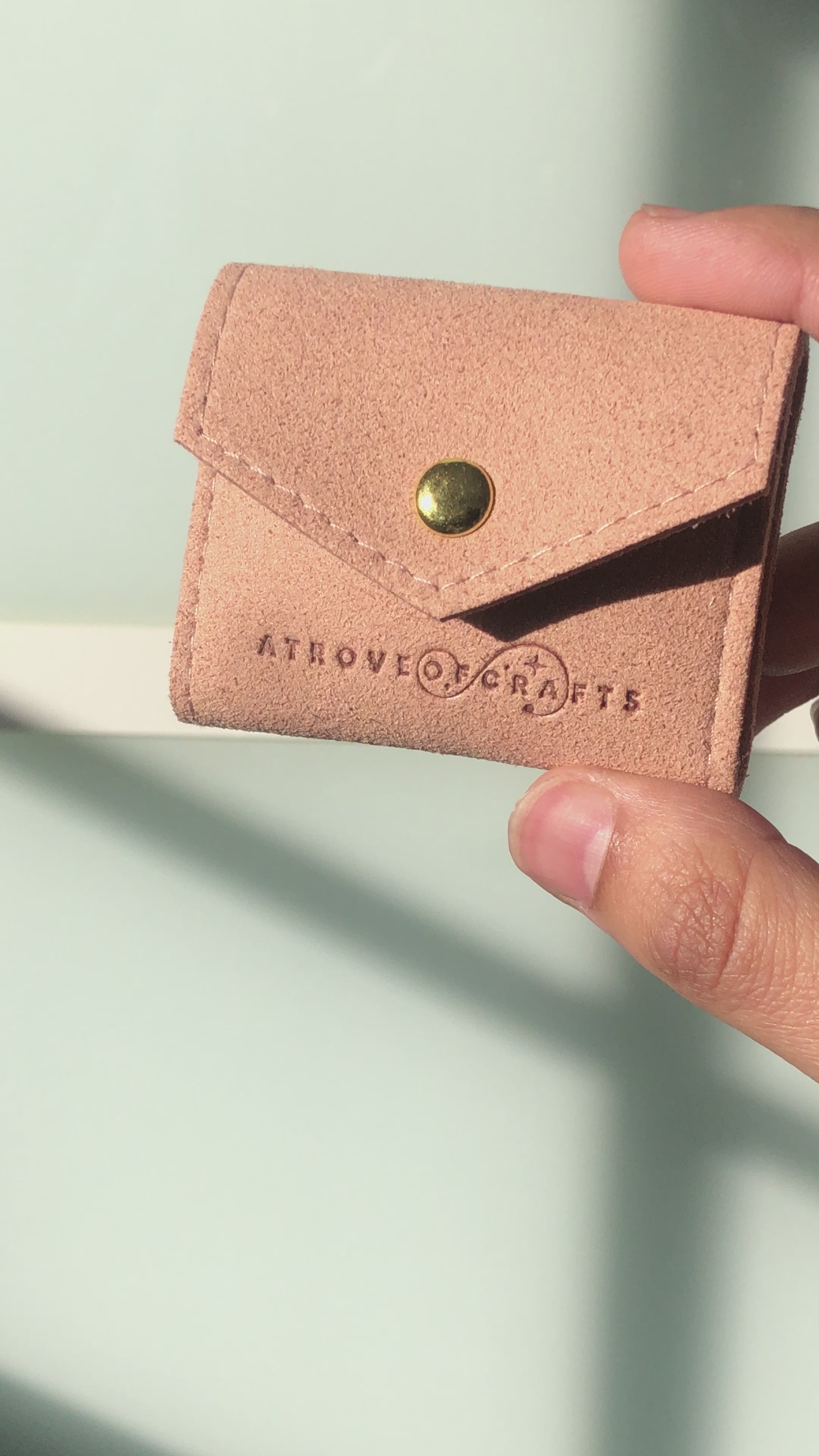 Travel sized light pink pouch with a brand logo on a red satin background